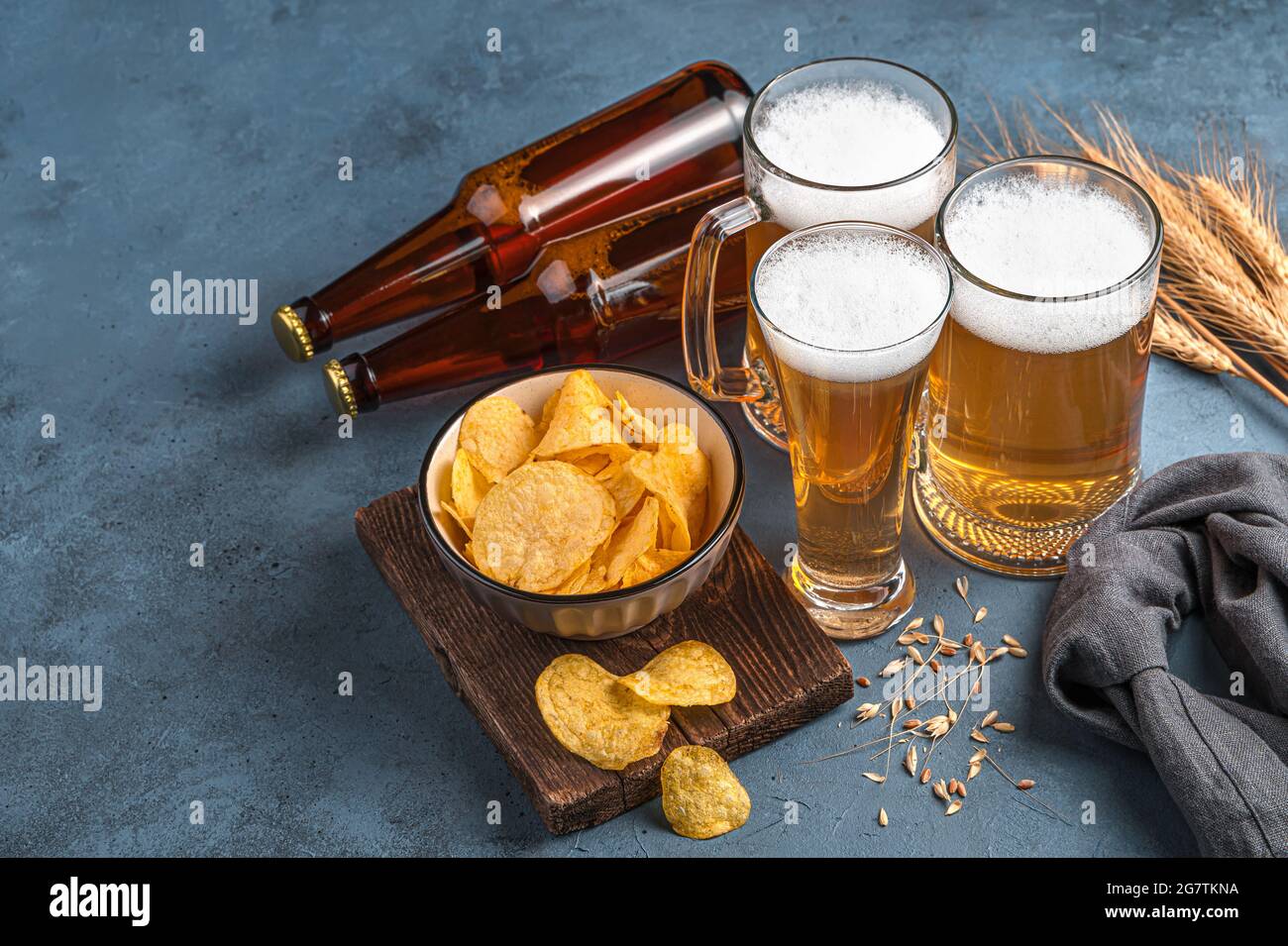 Bierbecher und -Flaschen, Chips und Weizen auf dunklem Hintergrund. Stockfoto