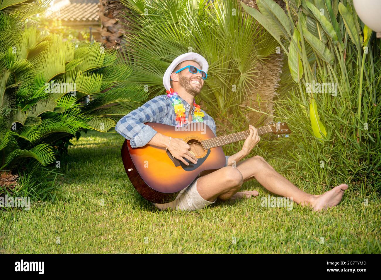 Porträt eines jungen, stilechten spielenden und singenden Mannes mit Gitarre in einem Garten Stockfoto