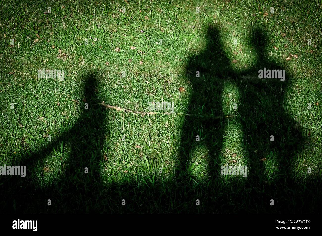 Schatten von drei Menschen werden durch das starke Sonnenlicht auf dem Gras reflektiert Stockfoto