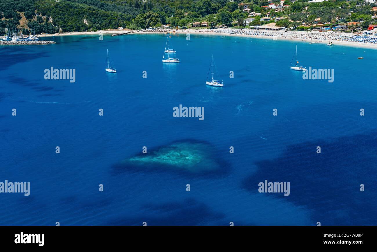 Mediterrane tiefblaue Meeresbucht mit herzförmigem seichtem Wasser, Segelyachten und sandiger Küste Stockfoto