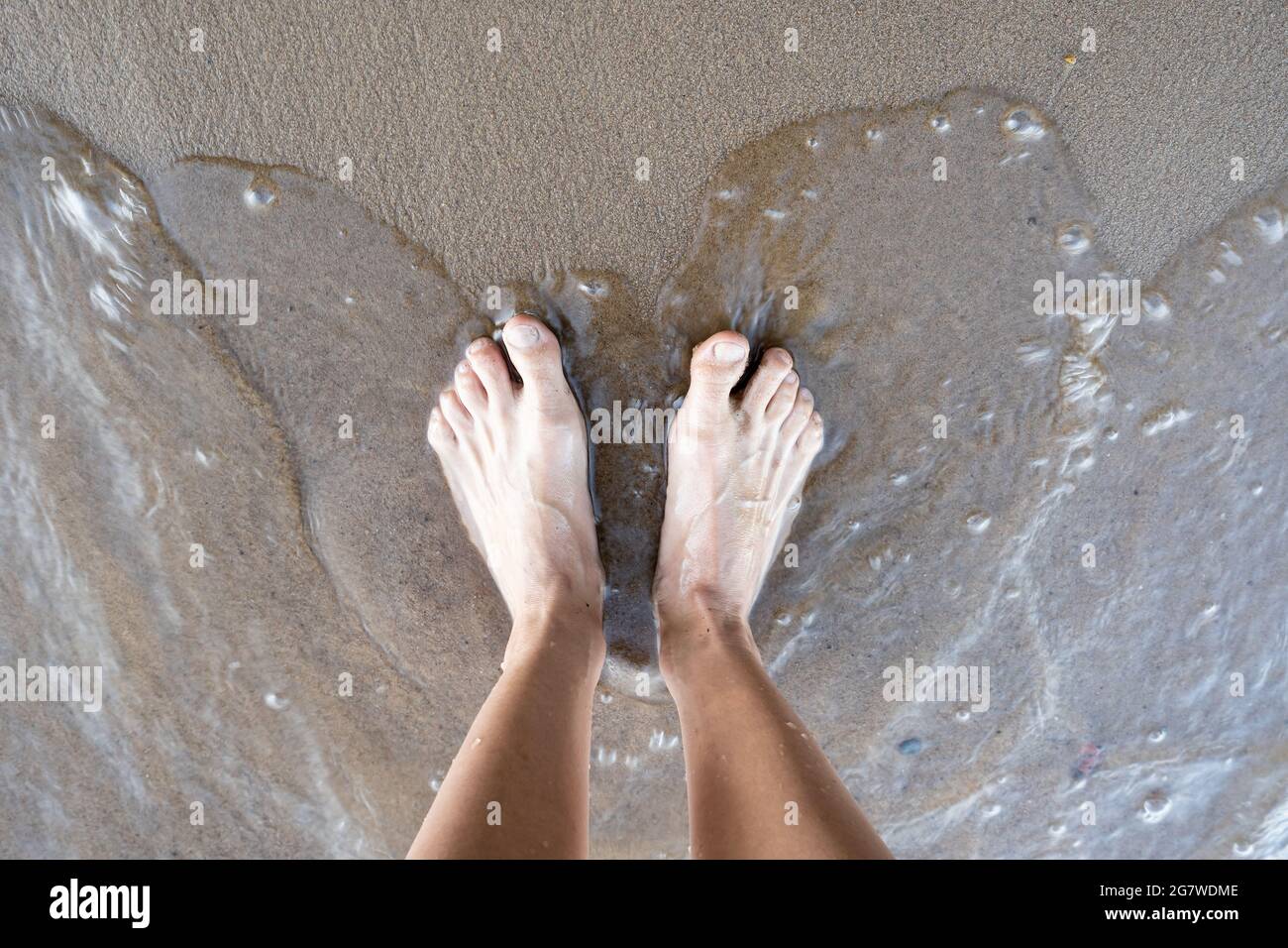 Frauen gebräunte Beine stehen im Wasser, am sandigen Ufer des Flusses, an einem Sommertag. Lifestyle. Draufsicht. Stockfoto