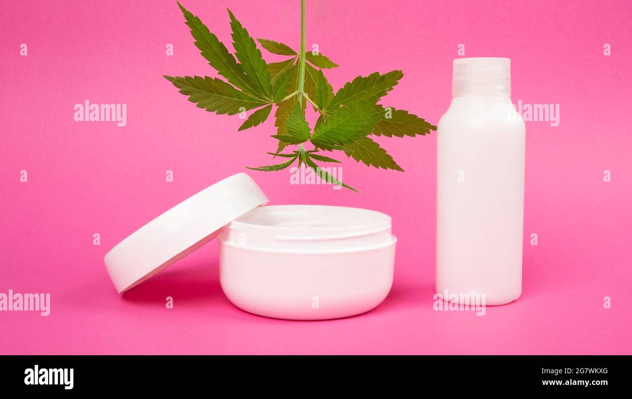 Hautpflegekosmetik mit Marihuanaextrakt auf rosafarbenem Hintergrund, verjüngende Creme mit Cannabisblatt. Stockfoto