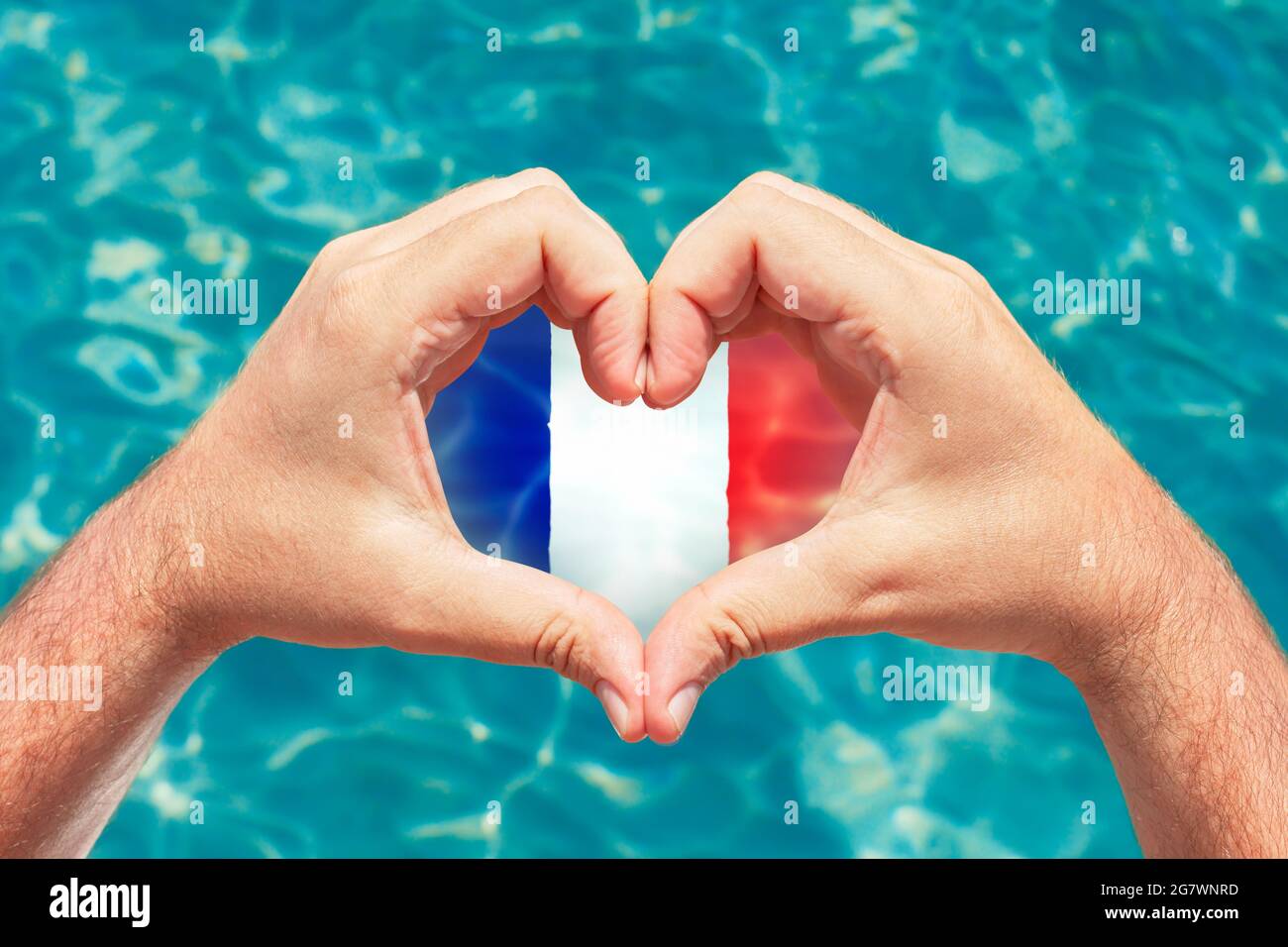 Sommerurlaub in Frankreich Konzept. Männliche Hände, die Herzform mit Frankreich-Flagge im Inneren bilden. Wunderschönes kristallklares türkisfarbenes Wasser mit Ätzstoffen. Stockfoto