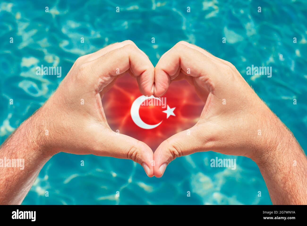Sommerurlaub in der Türkei Konzept. Männliche Hände, die Herzform mit Türkei-Flagge im Inneren bilden. Wunderschönes kristallklares türkisfarbenes Wasser mit Ätzstoffen. Stockfoto