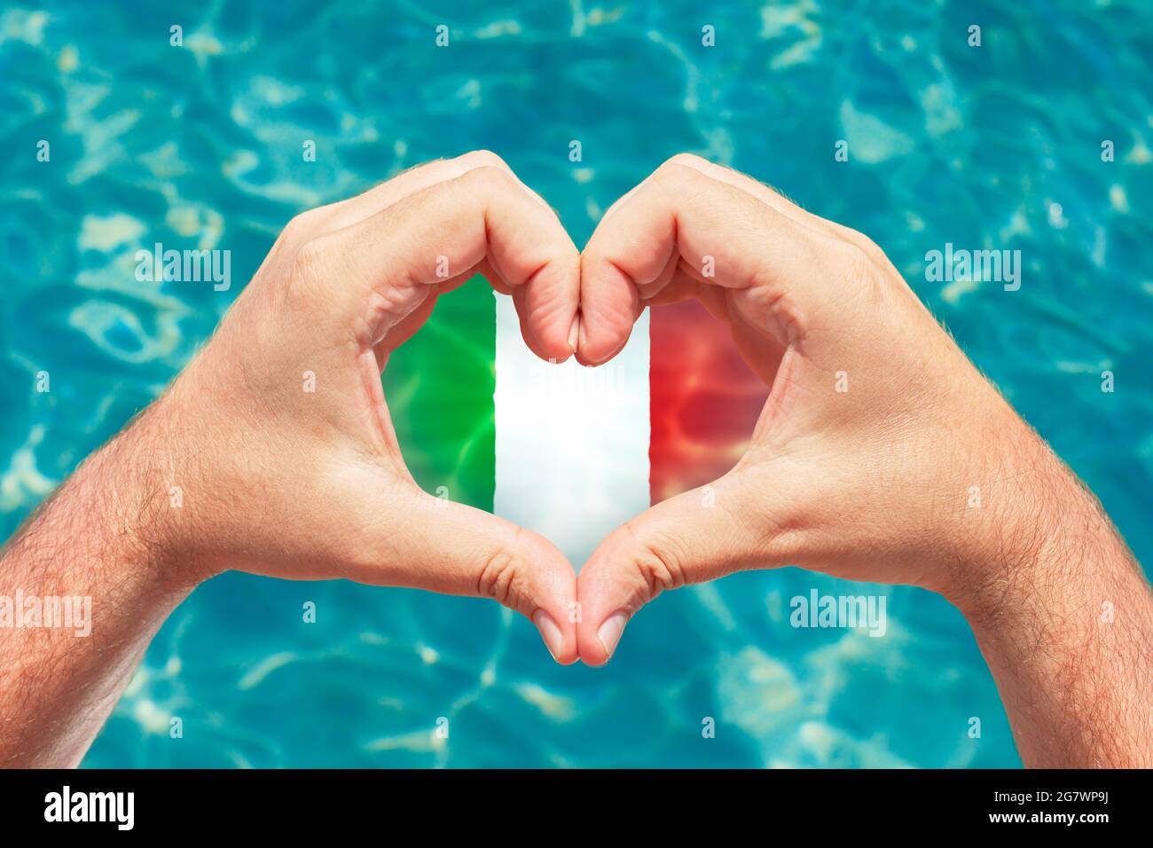 Sommerurlaub in Italien Konzept. Männliche Hände machen Herzform mit Italien Flagge innen. Wunderschönes kristallklares türkisfarbenes Wasser mit Ätzstoffen. Stockfoto