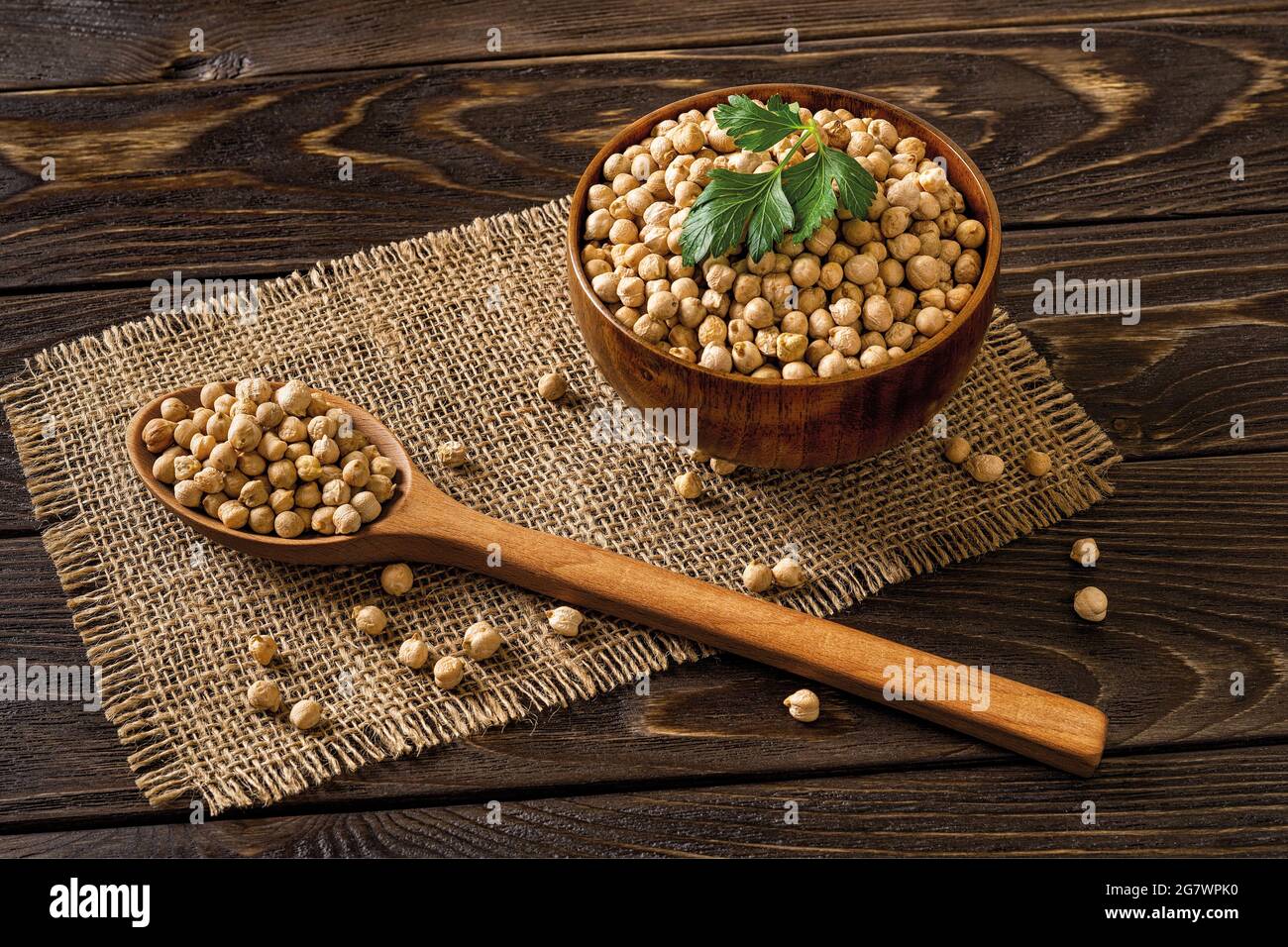 Holzschüssel und großer Löffel, beide voller roher Kichererbsen, über einem schwarzen rustikalen Tisch. Low-Key-Bild der trockenen Zutat von Hummus. Ballaststoffe. Stockfoto