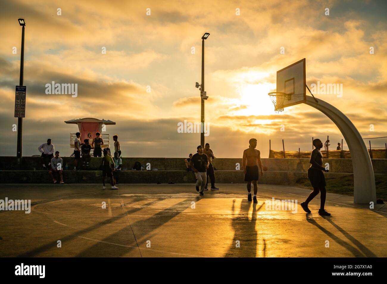 Männer spielen Basketball bei Sonnenuntergang auf einem Basketballplatz im Freien Stockfoto