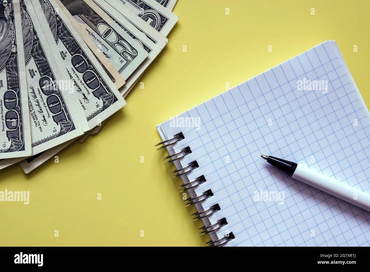 Geschäftselemente - Geldfan, weißes Notizbuch, Kugelschreiber auf gelbem Hintergrund. Banknoten verschiedener Stückelungen. Draufsicht. Selektiver Fokus. Nahaufnahme. Stockfoto