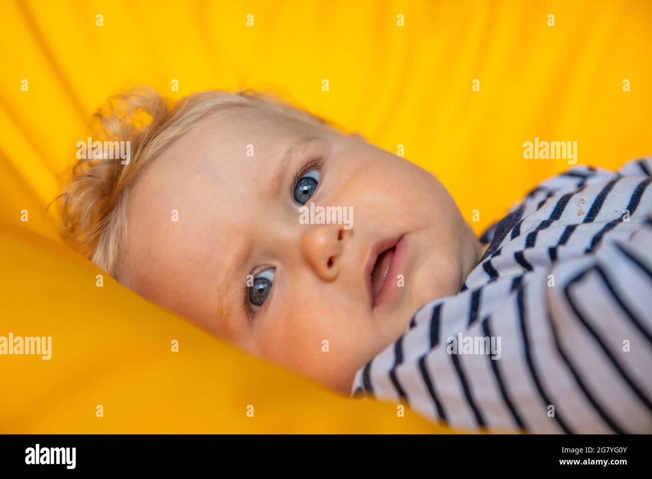 Nahaufnahme eines niedlichen 9 Monate alten Jungen mit blauen Augen auf einem gelben Hintergrund Stockfoto