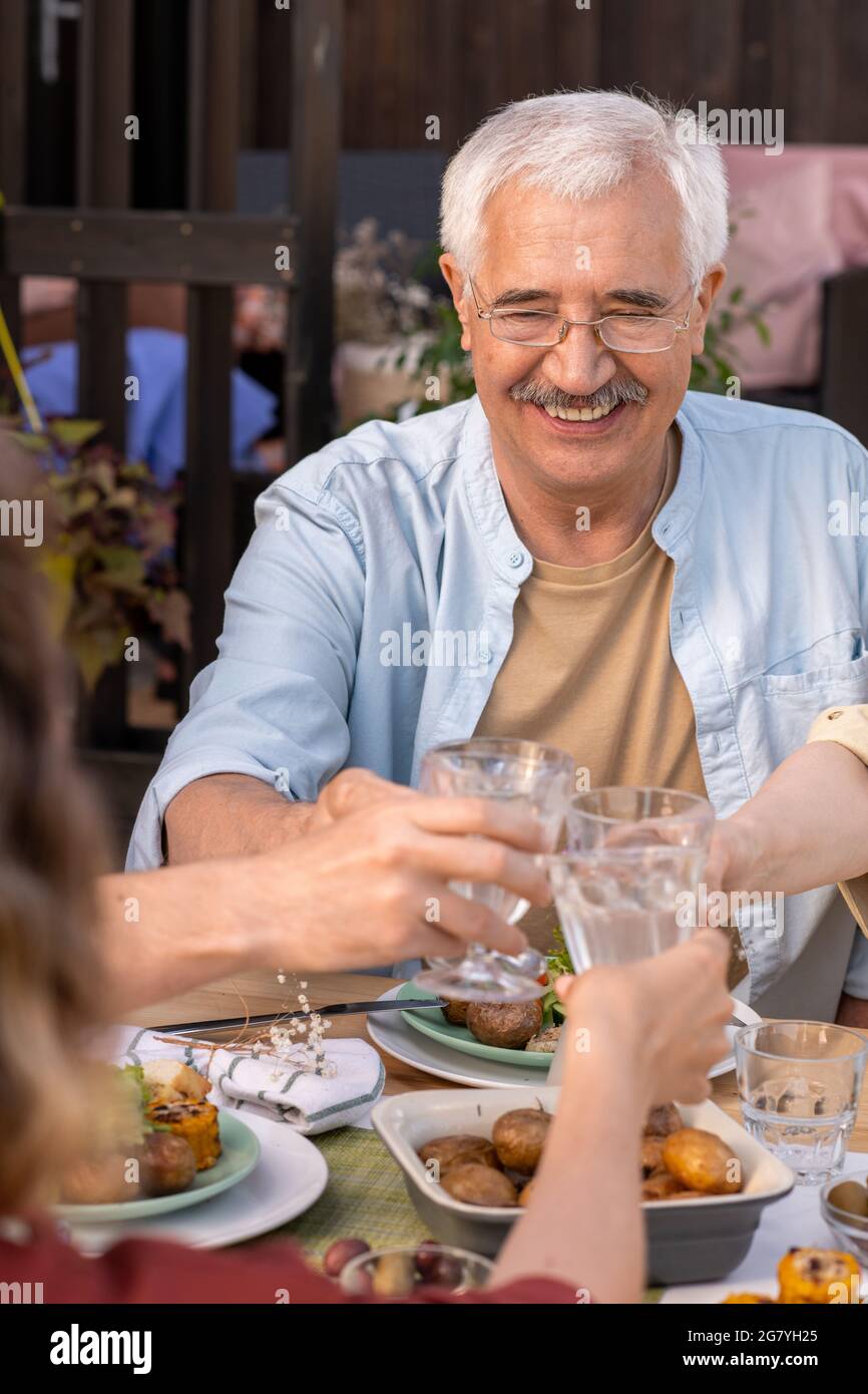 Porträt eines lächelnden älteren Mannes, der beim Geburtstagsessen mit Mitgliedern seiner Familie eine Brille anklickte Stockfoto