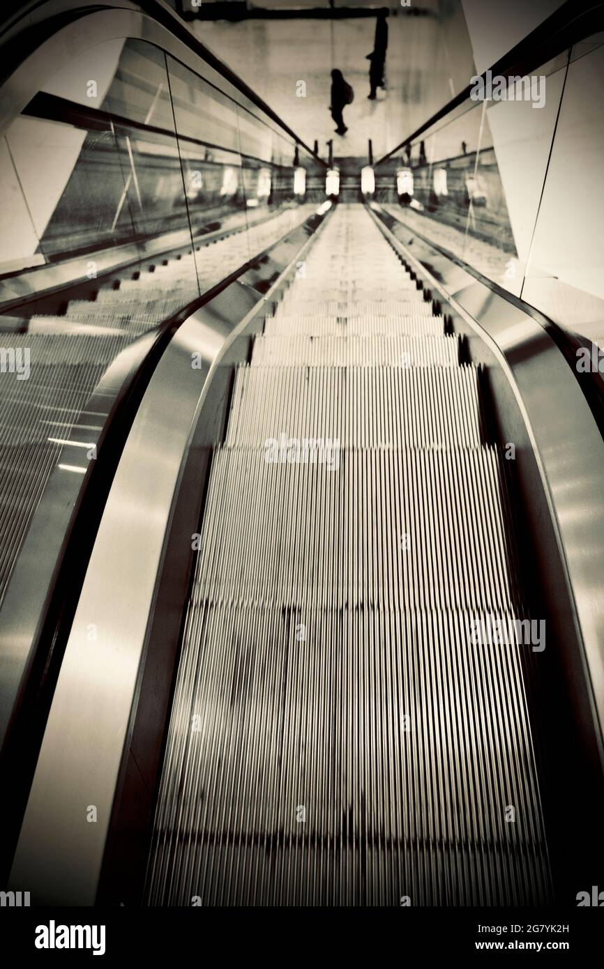 Rolltreppe im Bürogebäude mit drei Personen, starken perspektivischen Linien, Blick nach unten. Stockfoto