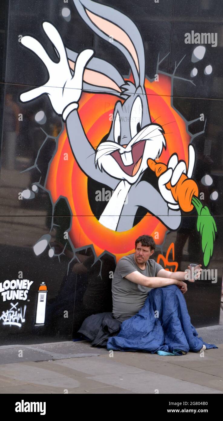 Ein Mann sitzt mit einer Tasse in der Luft in der Nähe eines Bugs Bunny-Bildes, Teil eines Looney Tunes-Kunstpfades, der in Manchester, England, Großbritannien, eröffnet wurde. Stockfoto