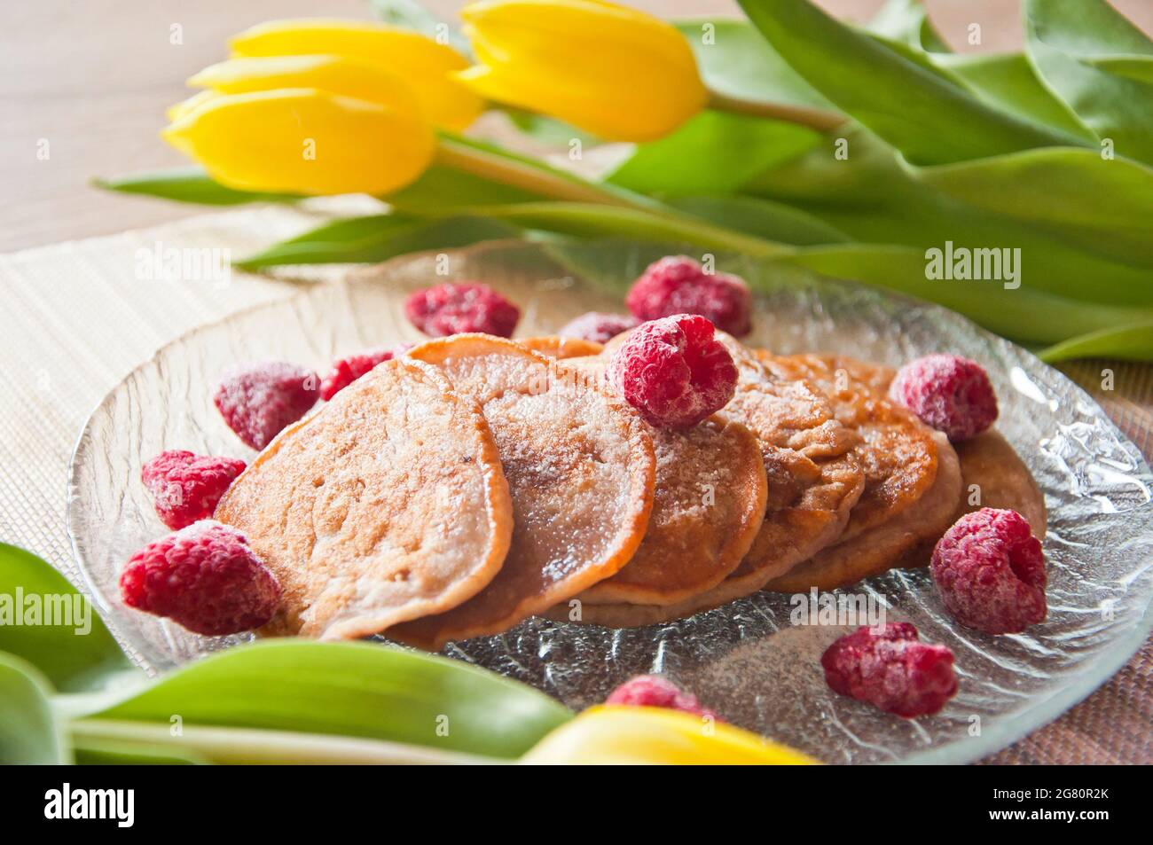 Ein paar leckere hausgemachte Bananenpasteten mit gefrorenen Himbeeren mit gelben Tulpen und Bananen im Hintergrund Stockfoto
