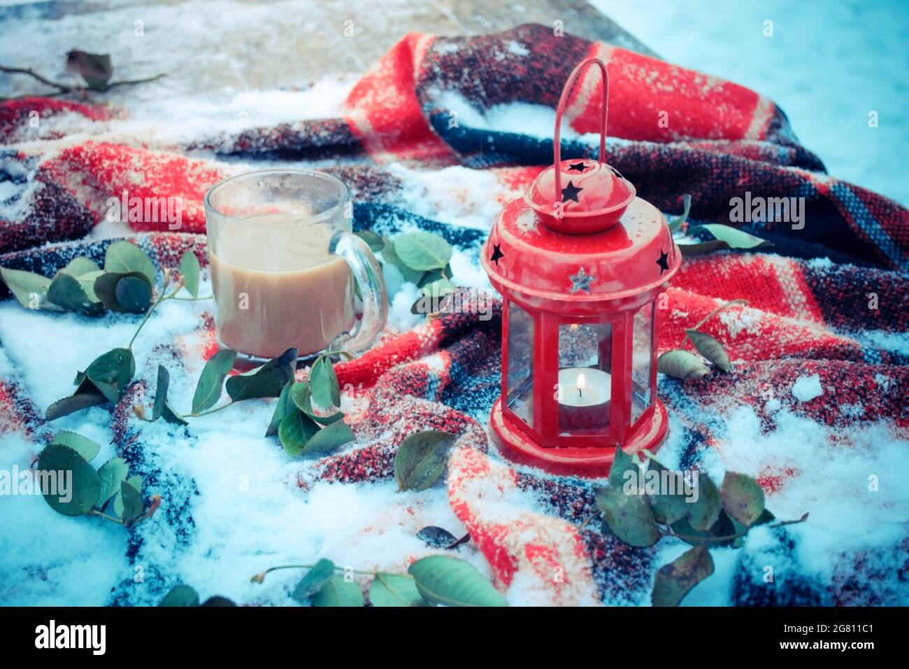 Festliche rote Kerze in Laterne und Tasse Kaffee auf Teppich mit Schnee Stockfoto