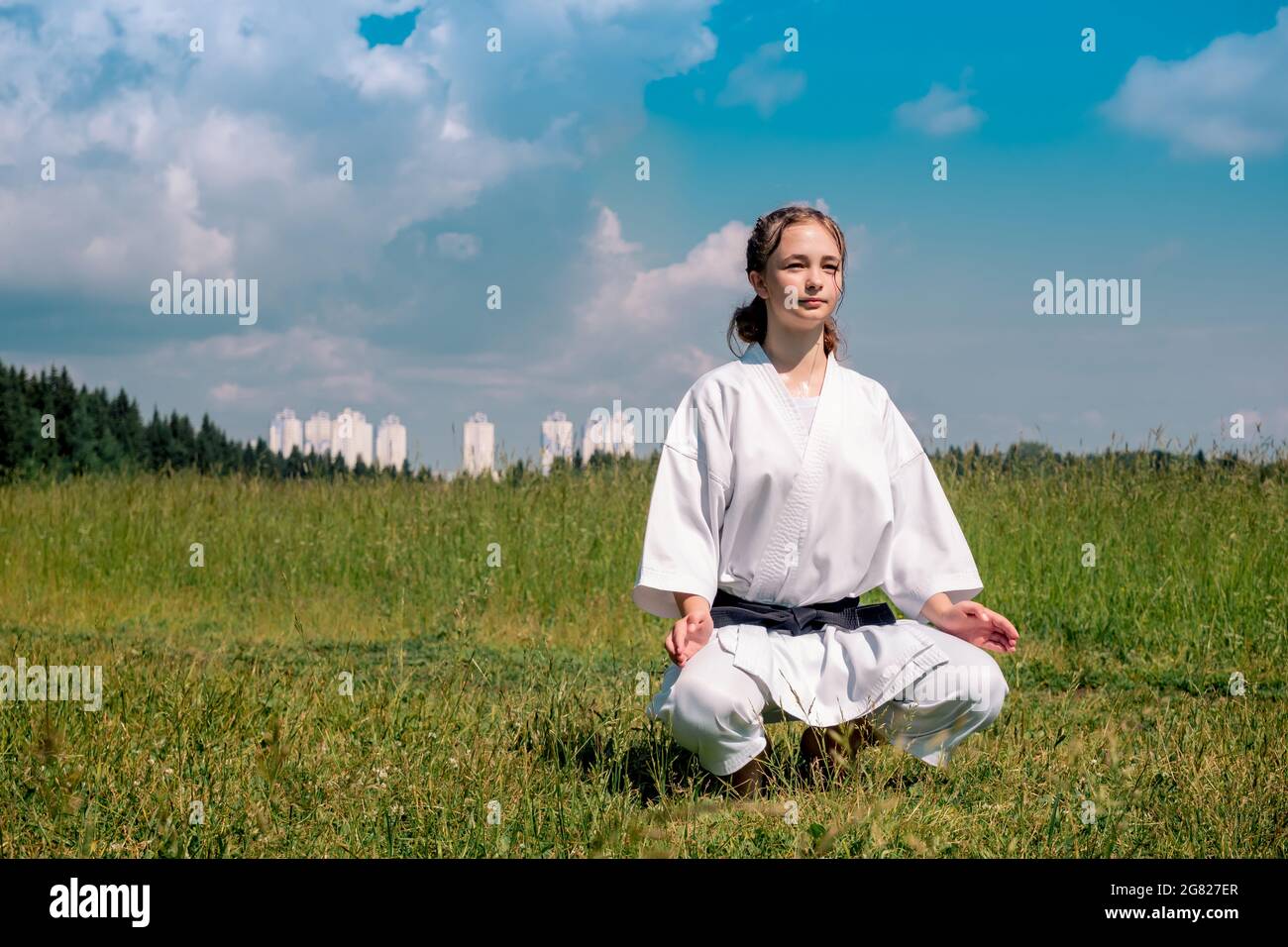 Teenager-Mädchen Karateka vor Beginn des Trainings im Freien tritt in den Mokuso-meditativen Zustand in der Seiza-Pose Stockfoto