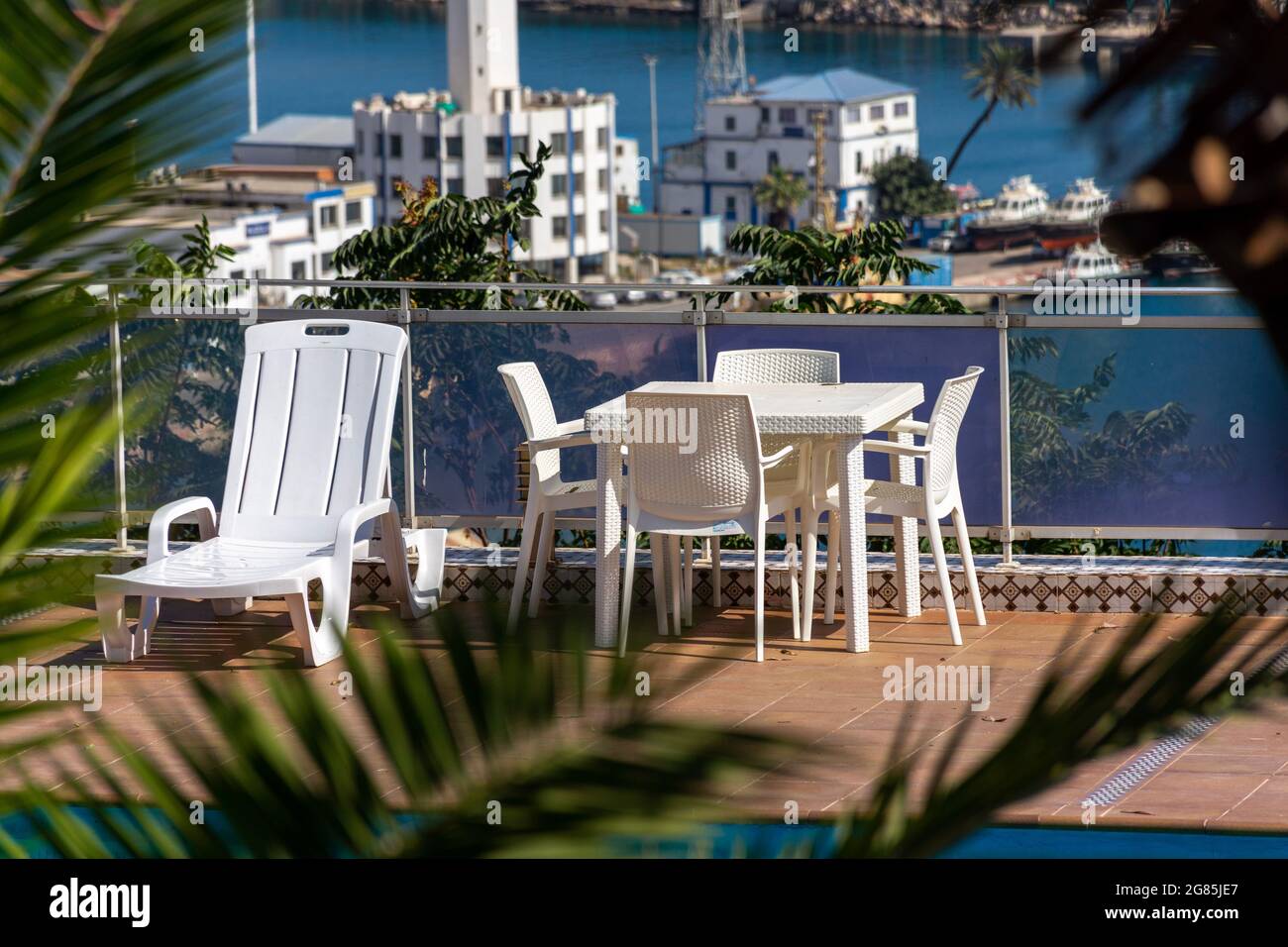 Weiße Plastikstühle mit Tisch und Sonnenliegen in der Nähe des Pools. Stockfoto
