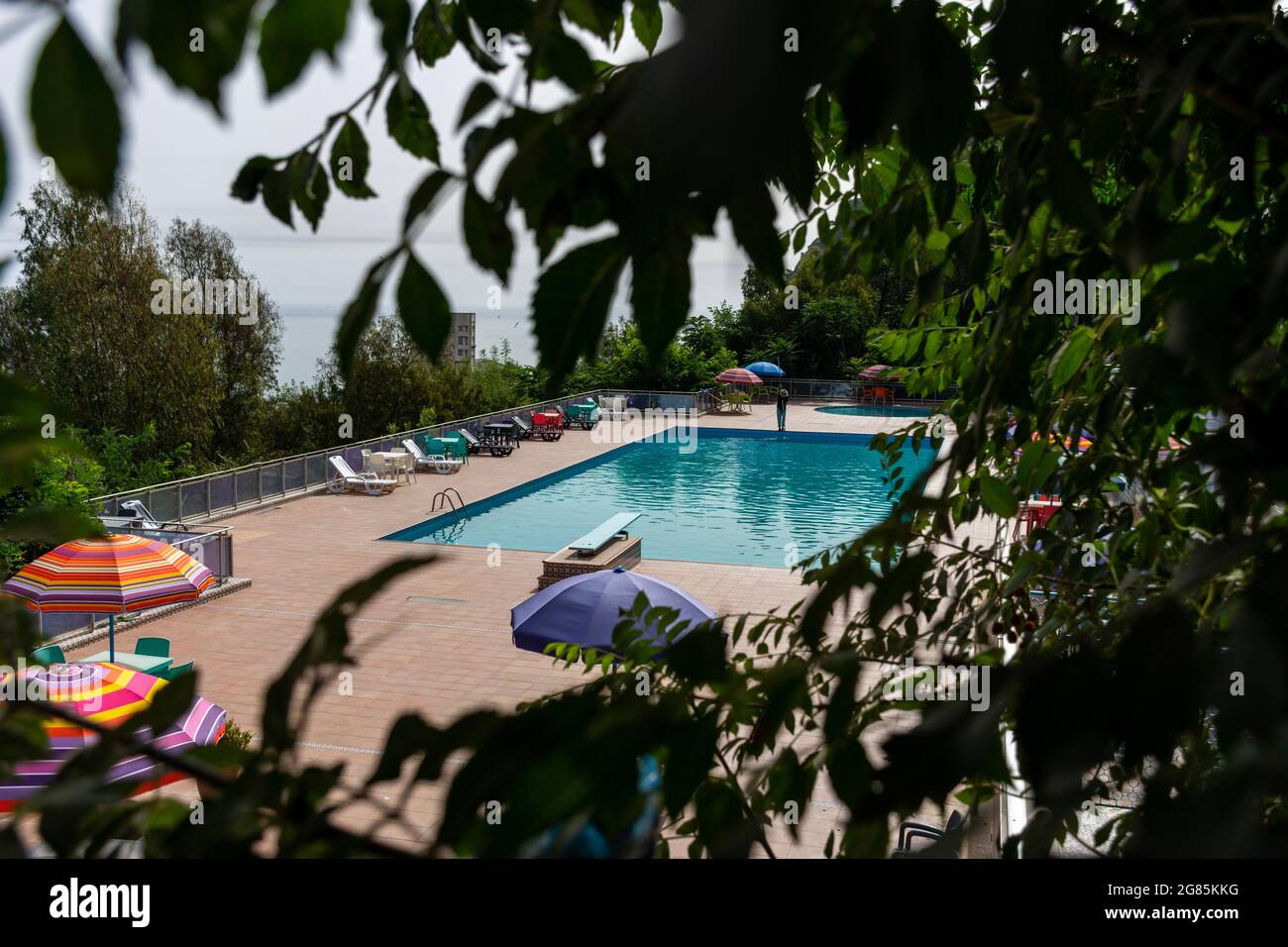 Mann, der den Pool putzte, bunte Sonnenschirme und Sonnenliegen. Stockfoto