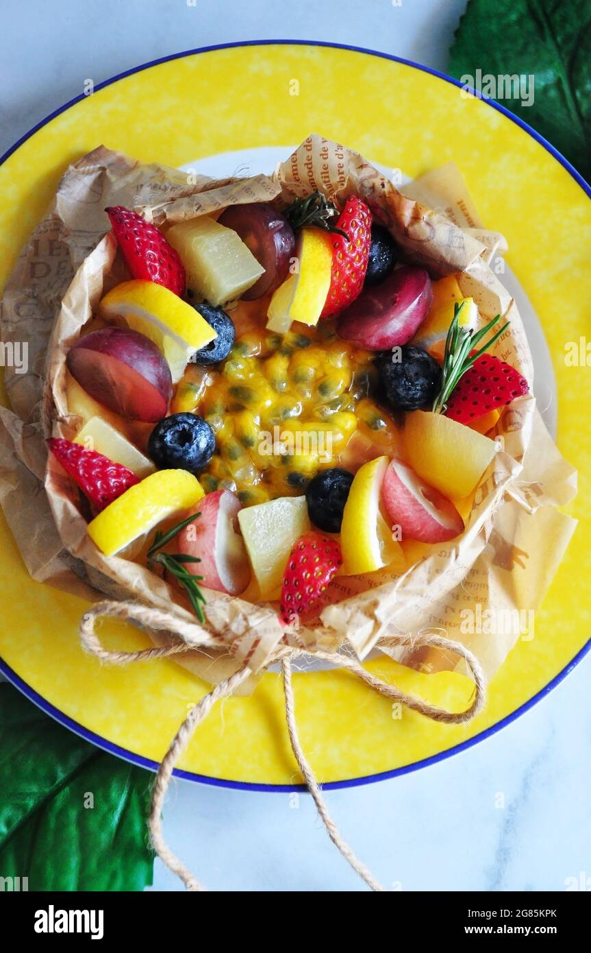 Oben von Sommerfrüchten und Passionsfrucht-Sauce oben auf Käsekuchen servieren auf gelber Schale Stockfoto