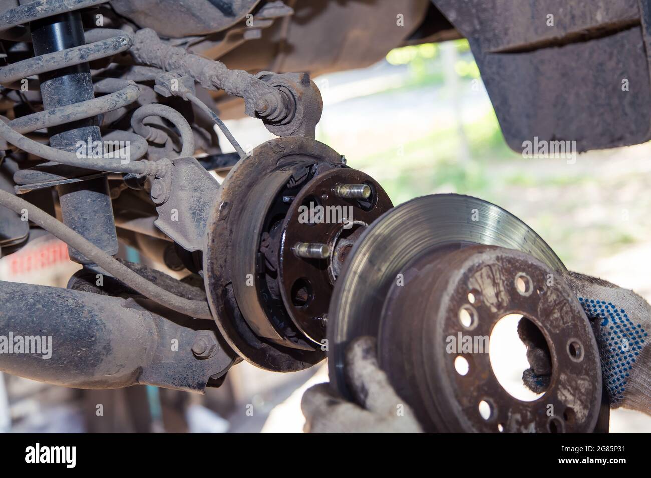 Mit Handschuhen entferne oder schiebe die Felge auf die Nabe des alten Autos. In der Garage wechselt ein Mann Teile an einem Fahrzeug. Konzept für kleine Unternehmen, Reparatur- und Wartungsservice für Fahrzeuge. UHD 4K. Stockfoto