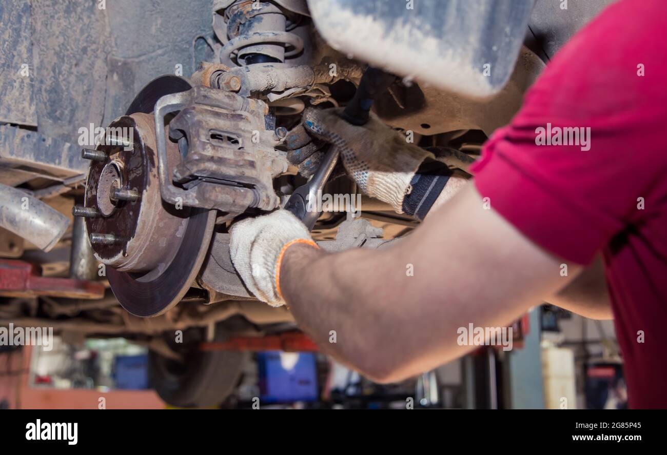 Mit männlichen Händen wird die Radstütze des alten Fahrzeugs mit einem Schraubenschlüssel befestigt oder abschrauben. In der Garage wechselt ein Mann Teile an einem Fahrzeug. Konzept für kleine Unternehmen, Reparatur- und Wartungsservice für Fahrzeuge. UHD 4K. Stockfoto