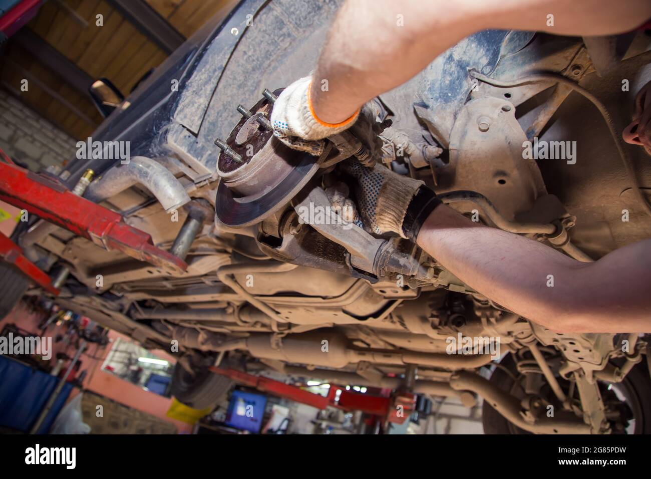 Mit Handschuhen geratende männliche Hände montieren oder entfernen den Bremssattel am Rad eines alten Autos. In der Garage wechselt ein Mann Teile an einem Fahrzeug. Konzept für kleine Unternehmen, Reparatur- und Wartungsservice für Fahrzeuge. UHD 4K. Stockfoto