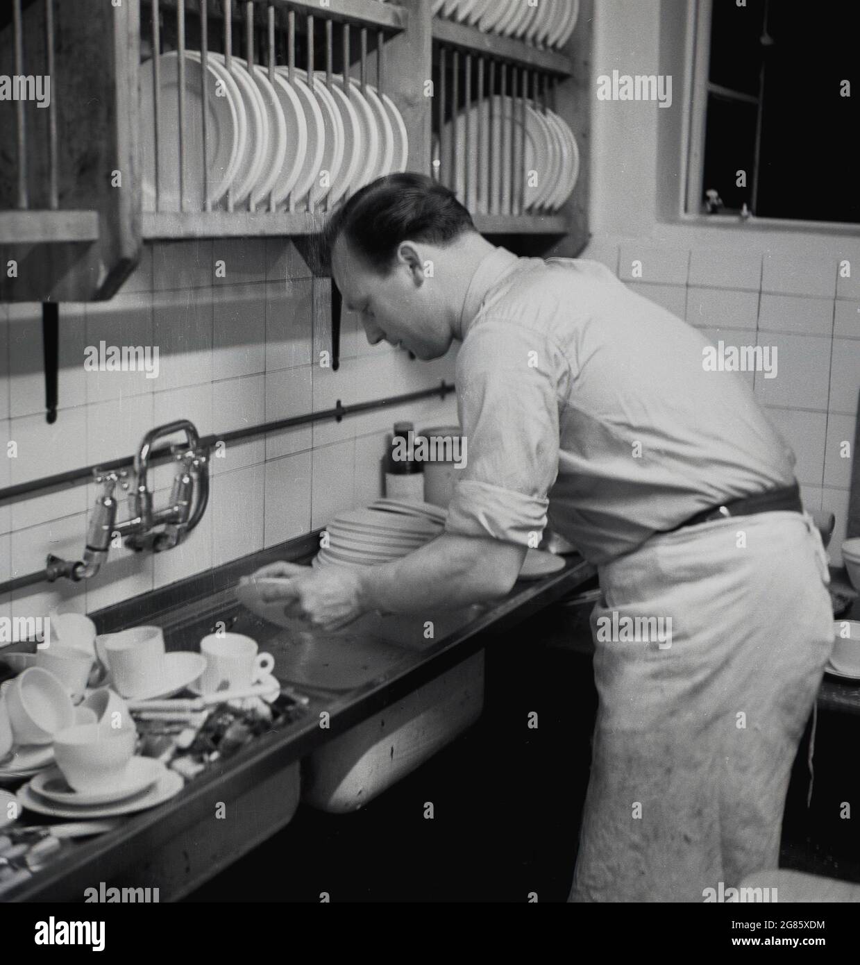 50er Jahre, historisch, Spülen... ein männlicher Kaffeehausbesitzer, der  sich über ein Waschbecken beugte und das gebrauchte Geschirr in einem  kleinen, engen Küchenbereich, Engand, Großbritannien, spülte  Stockfotografie - Alamy