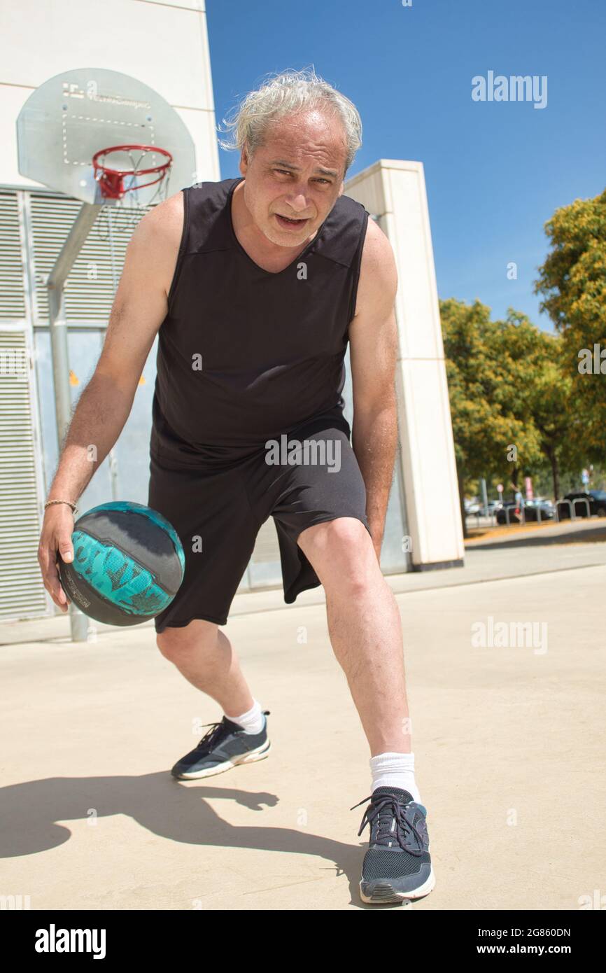 Nahaufnahme eines reifen Mannes, der allein auf einem Basketballplatz auf der Straße Basketball spielt Stockfoto