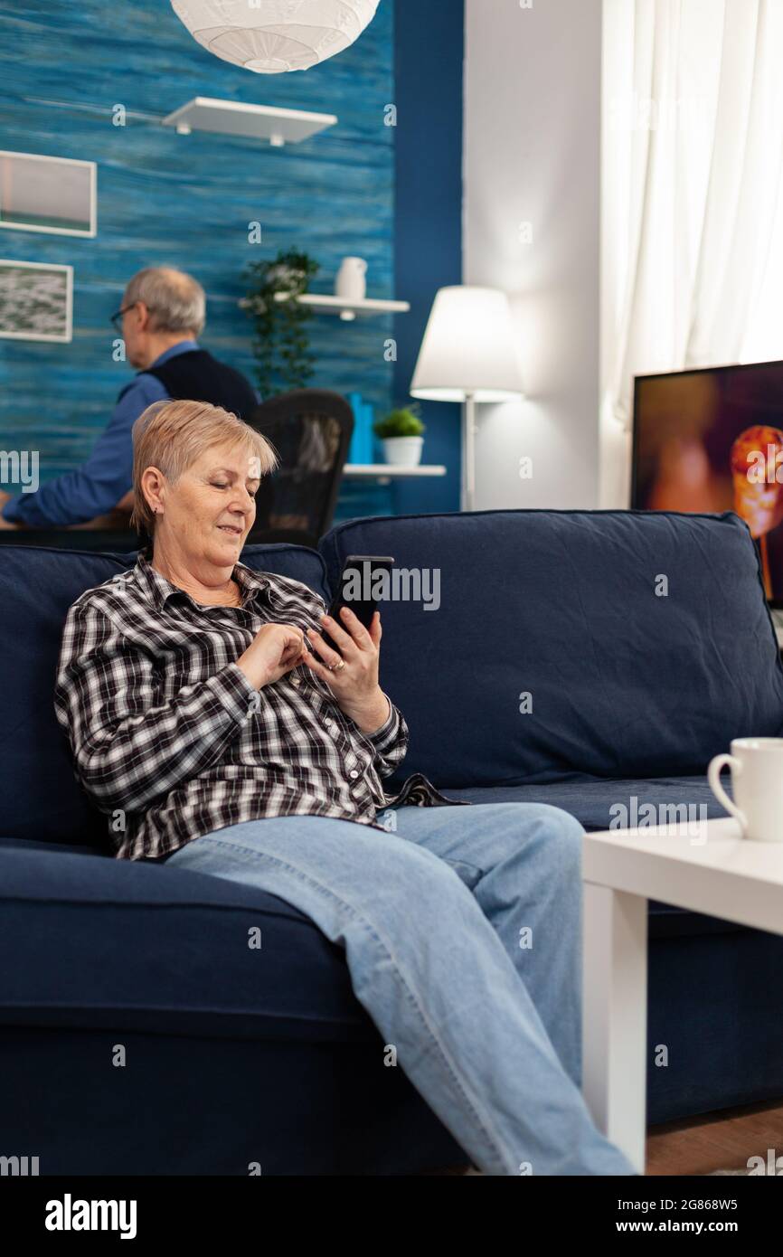 Hapy ältere Dame SMS am Telefon entspannen auf dem Sofa genießen Ruhestand Lebensstil. Ältere Frau im Internet surfen mit Smartphone sitzen auf dem Sofa im Wohnzimmer zu Hause. Stockfoto