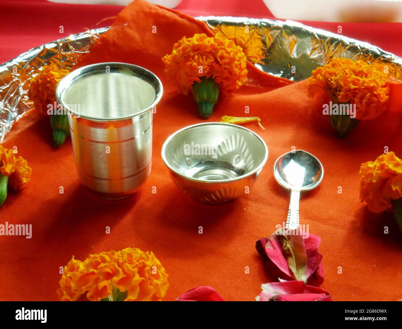 Indische traditionelle Anbetung Silbermetallglas und Löffel religiöse  Besteck mit Ringelblumen auf Deep Safran Stoff präsentiert Stockfotografie  - Alamy