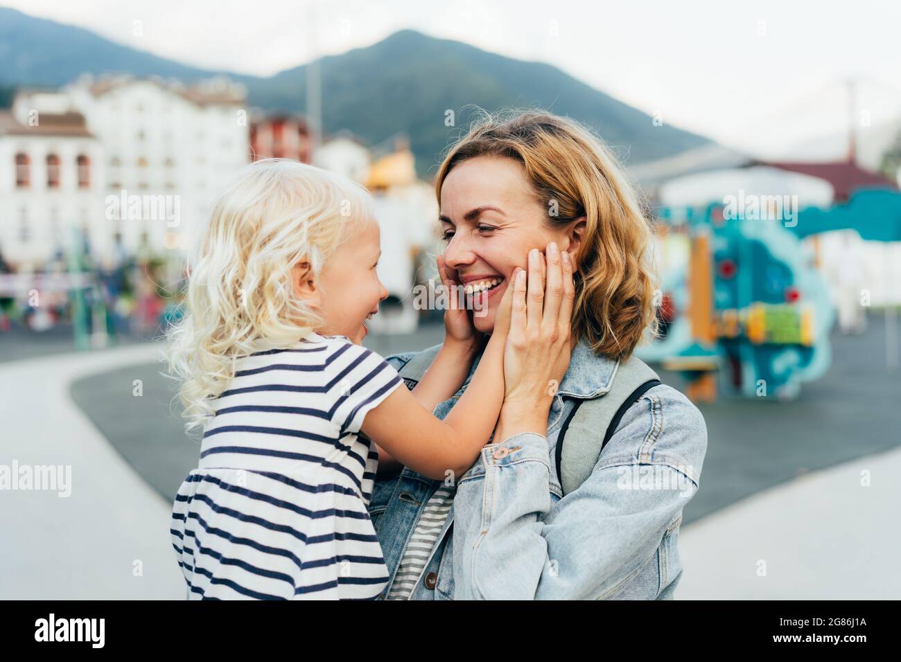 Die kleine Tochter berührt und umarmt das Gesicht ihrer Mutter mit ihren Handflächen. Liebe zu Mutter und Kind. Stockfoto