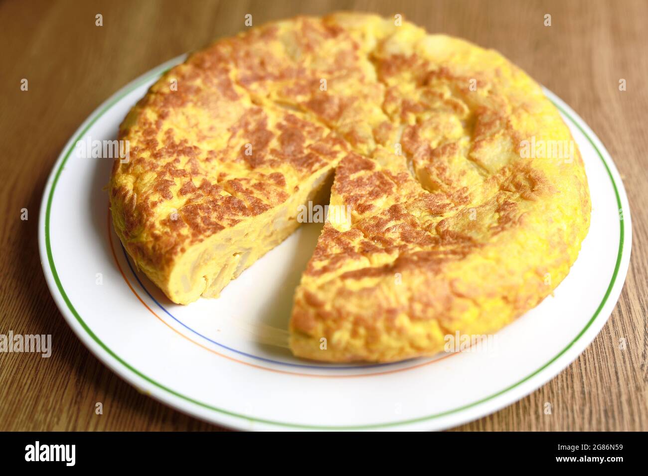 Hausgemachtes spanisches Omelett auf einem weißen Teller, auf dem Hintergrund eines Holztisches. Stockfoto