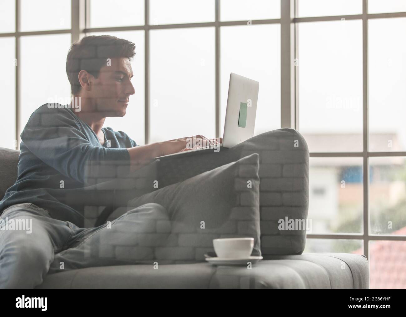 Junger und hübscher kaukasischer Geschäftsmann in lässigem Stoff, der glücklich sitzt Auf dem Sofa und mit Laptop kommunizieren Notebook-Computer mit dem Außerhalb AA Stockfoto