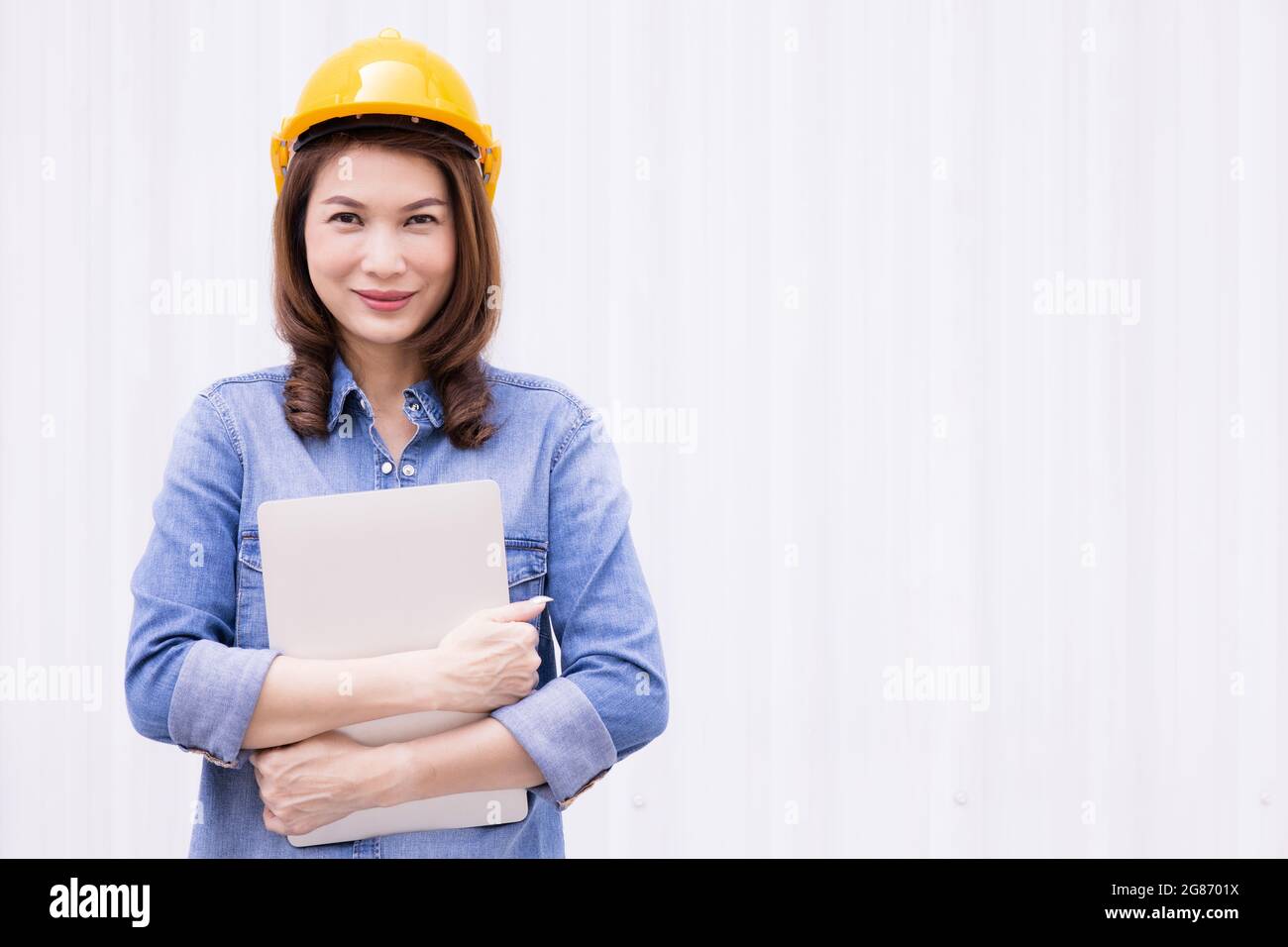 Schöne asiatische weibliche Ingenieur in Jeans Kleid tragen gelbe Sicherheit Hard hat mit Laptop-Computer Notebook Arbeit bei der Konstruktion Standort außerhalb von Stockfoto