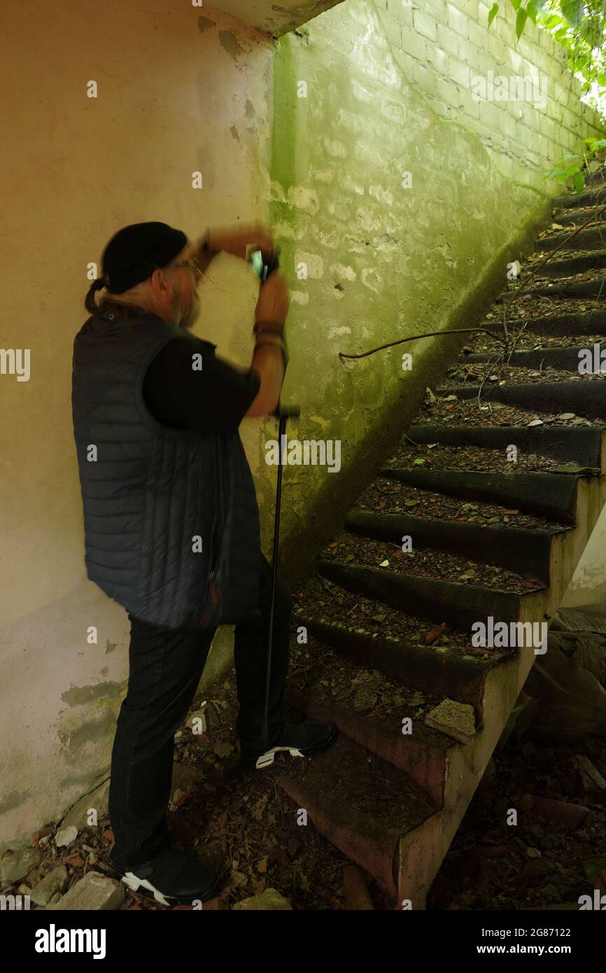 Ein älterer männlicher Fotograf, der ein Foto der beschädigten Treppe in einem verlassenen Gebäude auffängt. Stockfoto
