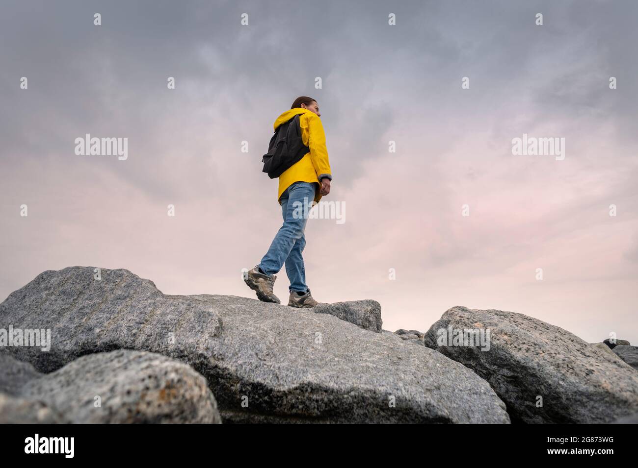 Rückansicht einer Backpacker-Frau in einer gelben Jacke, die über Felsen und Felsbrocken läuft und die Gegend erkundet. Stockfoto