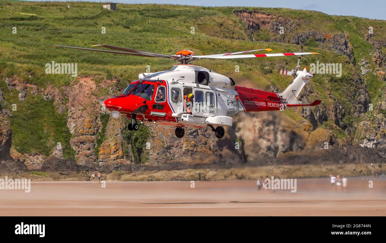 Lunan Bay Beach, Angus, Schottland, Großbritannien, 17. Juli 2021: Große Rettungsaktion der Küstenwache und RNLI, nachdem eine Mutter und Tochter heute am Lunan Bay Beach mit ihrem aufblasbaren Schlauchboot bei starkem Wind auf See getrieben wurden. Ein Offshore-Versorgungsschiff, das sich in der Nähe befand, startete ebenfalls seinen FRC, um bei der Rettung zu helfen. Auf diesem Foto können Sie den Küstenwache-Hubschrauber sehen, der am Strand an Land kommt, während einer der Hubschrauber-Crew aus der Tür schaut und Mitglieder der Öffentlichkeit darauf blicken. (Quelle: Barry Nixon/Alamy Live News) Stockfoto