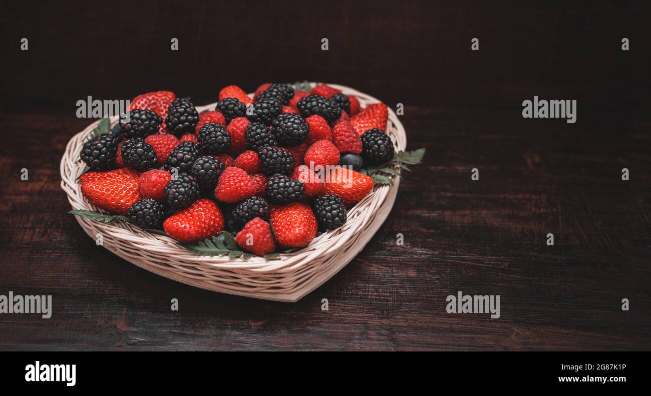 Beeren in einem Korb auf einem dunklen Holzhintergrund. Beerenmischung. Erdbeeren, Brombeeren und Himbeeren. Speicherplatz kopieren. Stockfoto