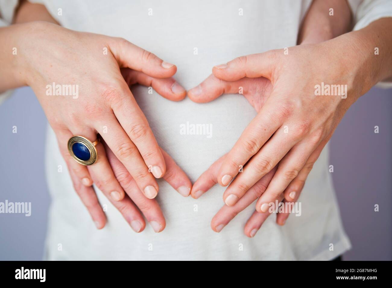 Schöne Nahaufnahme eines schwangeren Bäuches, sanft von liebevollen Händen gewiegt, symbolisiert die Verbindung zwischen Mutter und Baby. Die warme Beleuchtung und der weiche Fokus Stockfoto