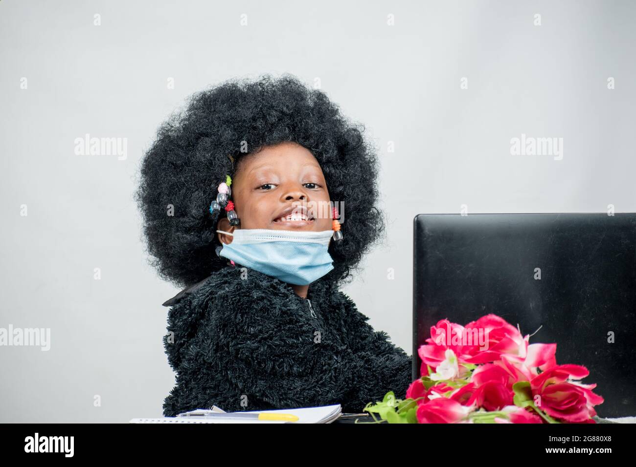 Afrikanisches Mädchenkind auf afro-Frisur mit Nasenmaske, studiert, lernt und liest allein für hervorragende Ausbildung mit einem Laptop Stockfoto