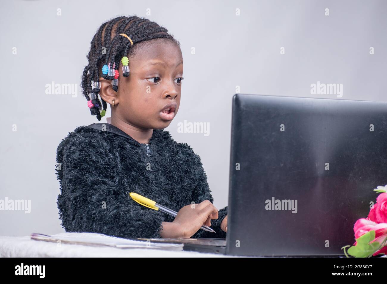 Afrikanisches Mädchen, das allein studiert, lernt, liest und forscht, um in ihrer Ausbildung mit einem Laptop, einer Blume und einem Jotter in ihrer Vorderseite hervorragende Ergebnisse zu erzielen Stockfoto