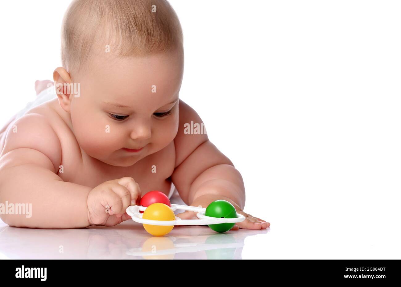 Fokussiertes Kleinkind Baby Baby Mädchen Kind in Windel liegt auf ihrem Bauch spielt mit Rassel, berühren mit der Hand Stockfoto