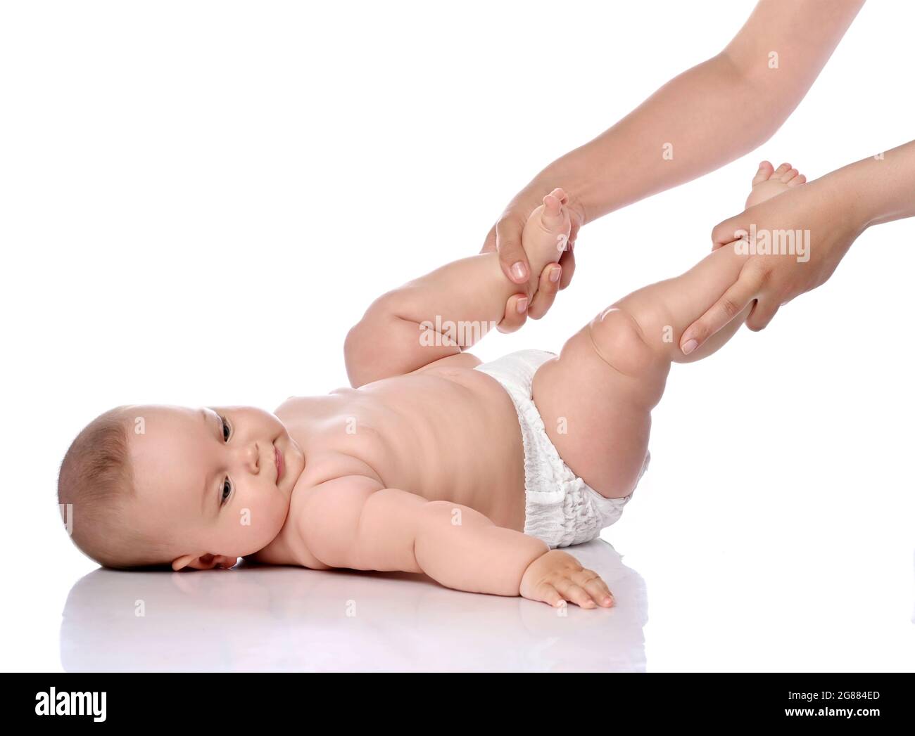 Ruhiges Kleinkind Baby Mädchen Kind in Windel liegt auf ihrem Rücken und macht Übungen, um Beine und Rückenmuskeln zu stärken Stockfoto