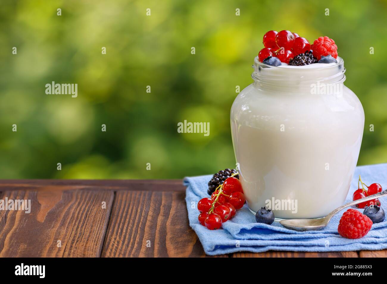 Joghurt mit frischen Beeren im Glas auf Holztisch im Freien Stockfoto