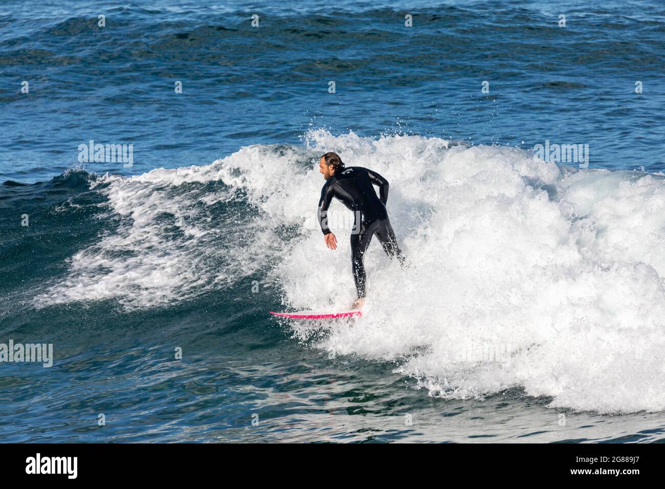 Australischer Mann im Neoprenanzug, der an einem Wintertag in Australien auf seinem Surfbrett im Avalon Beach Sydney die Wellen surft Stockfoto