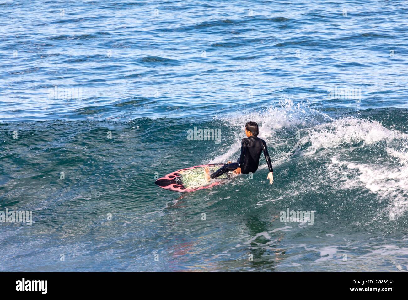 Australischer Mann im Neoprenanzug auf seinem Surfbrett, der an einem Wintertag an einem Strand in Sydney, NSW, Australien, die Wellen surft Stockfoto