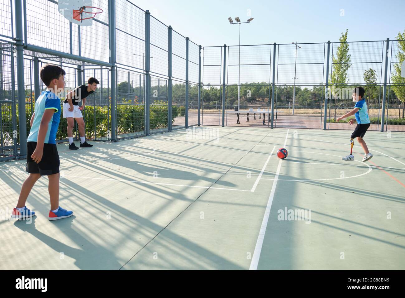 Drei Brüder spielen Fußball, einer von ihnen hat eine Beinprothese und tritt eine Strafe. Geschwister spielen zusammen Sport. Stockfoto