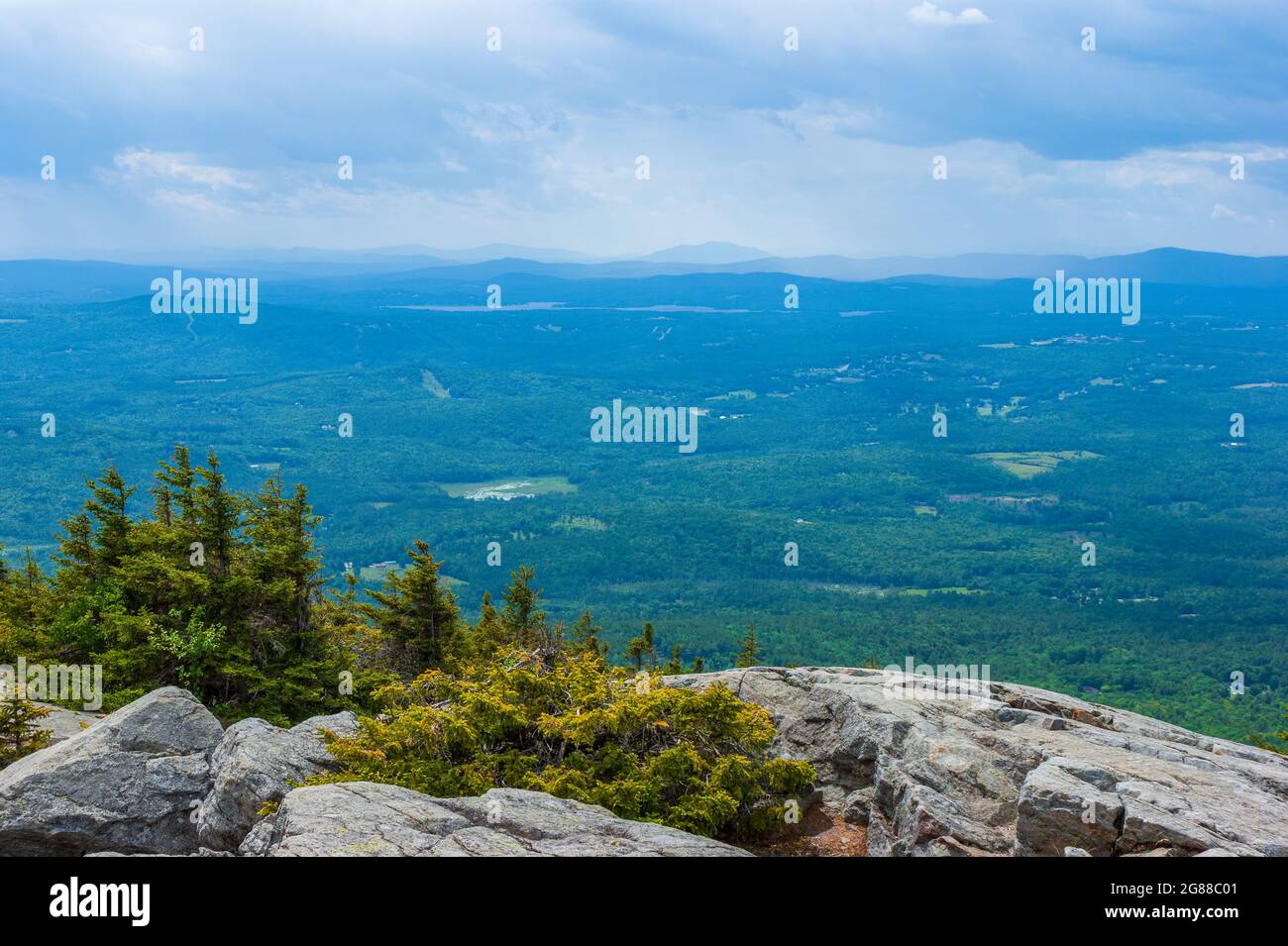 Blick auf den Westen vom Mt. Kearsarge Gipfel in Richtung Lake Sunapee und Mt. Ascutney. Felsiger Granitausschnitt und gestaute Fichtenbäume. Entfernte Gipfel und Grate Stockfoto