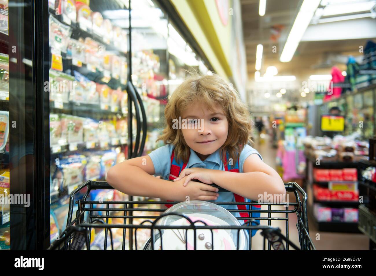 Kleines Kundenkind im Supermarkt oder Supermarkt mit Waren im Einkaufswagen. Stockfoto