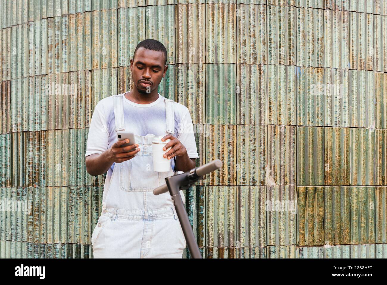 afrikanischer Pendler, der auf der Straße in der Nähe eines Rollers steht und sein Telefon benutzt Stockfoto