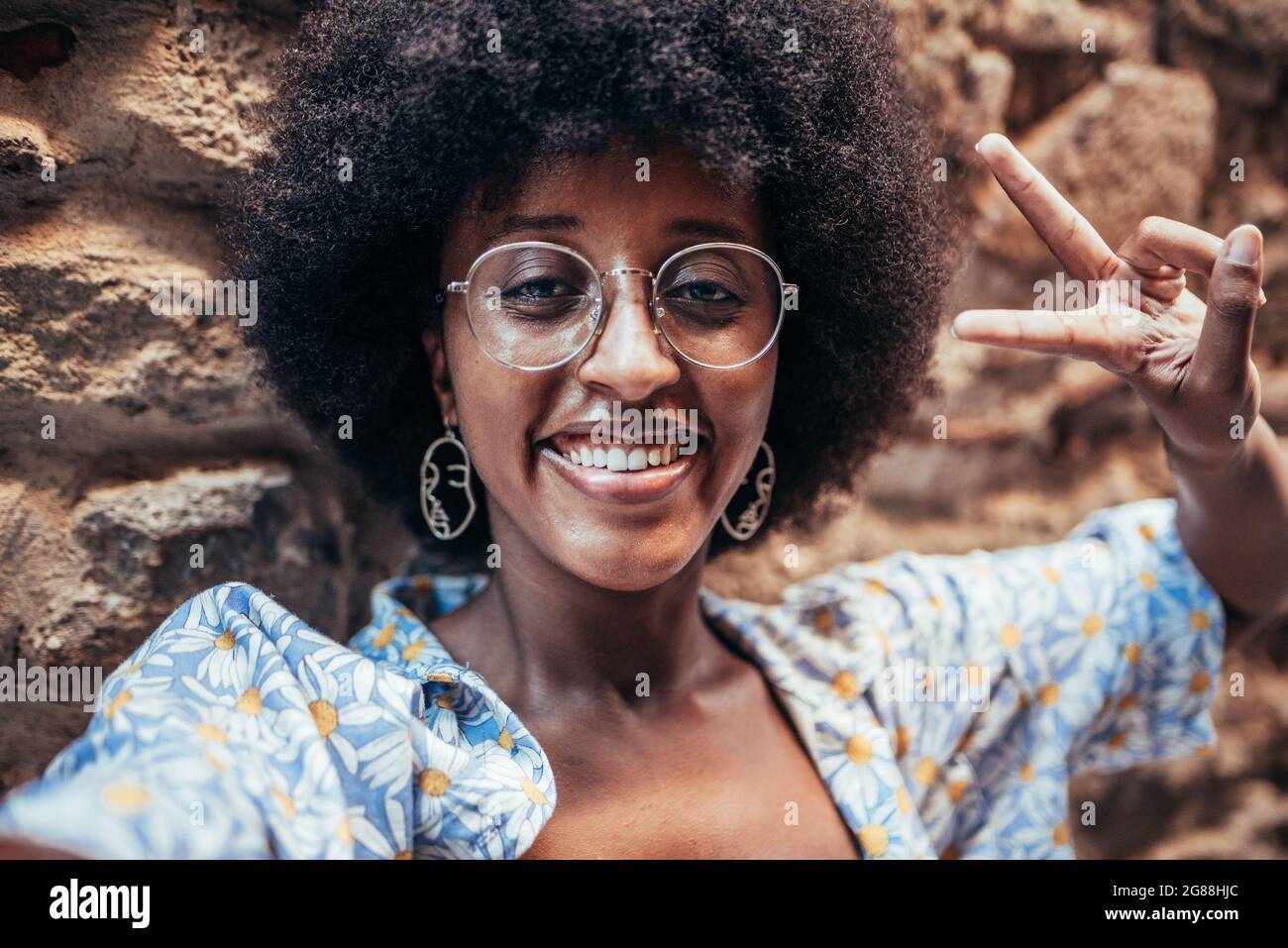 Selbstbild einer afrikanisch-fröhlichen Frau. Sie lächelt und tut mit ihren Fingern das Siegeszeichen. Konzept von Glück und Positivität Stockfoto